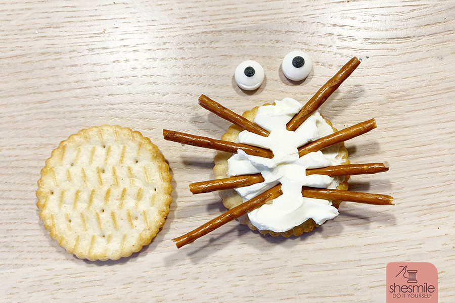 Alles was du brauchst sind Cracker-Kekse, Salzstangen, Augen und eine streichbare Creme. Damit erstellst du lustige Spinnen-Cracker für die Kinder-Halloween-Party. Eine Idee von shesmile.de