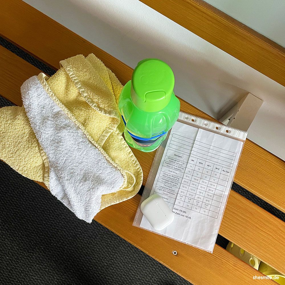 Meine Sportausstattung: Handtuch, Trinkflasche, Airpods und Trainingsplan